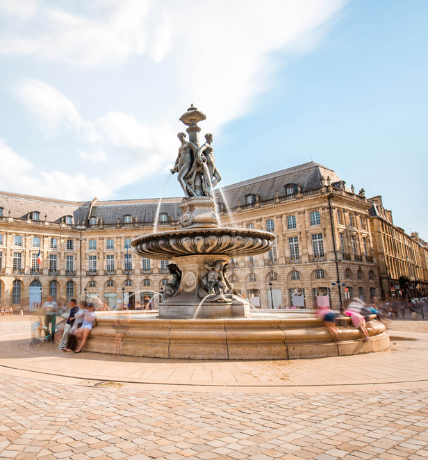 People sitting on the fountain at Place de la Bourse in Bordeaux, France on a sunny day